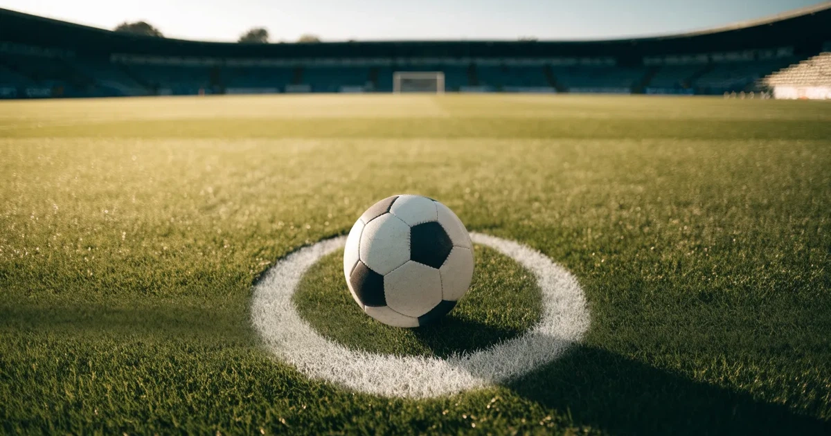 Uma bola de futebol no ponto central de um relvado, à luz da manhã