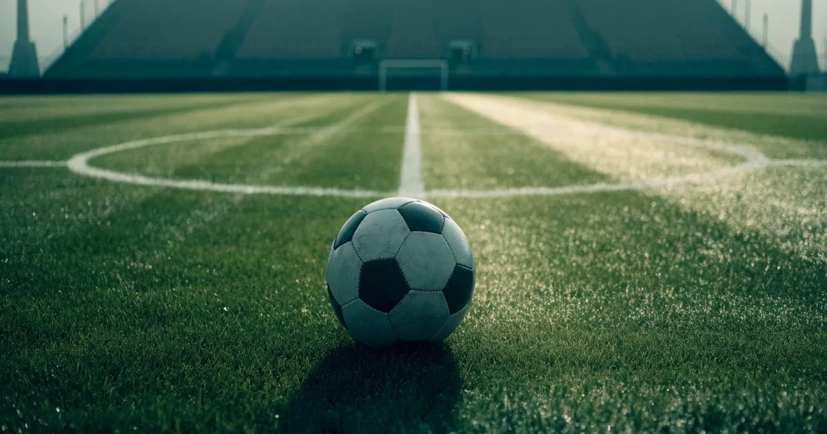 Uma bola de futebol no ponto central de um relvado, à luz da manhã